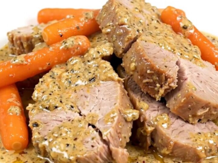 A close-up of sliced creamy ranch pork tenderloin and cooked baby carrots on a white plate.