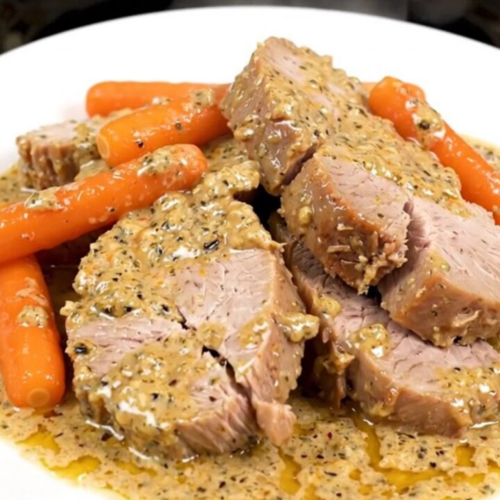 A close-up of sliced creamy ranch pork tenderloin and cooked baby carrots on a white plate.