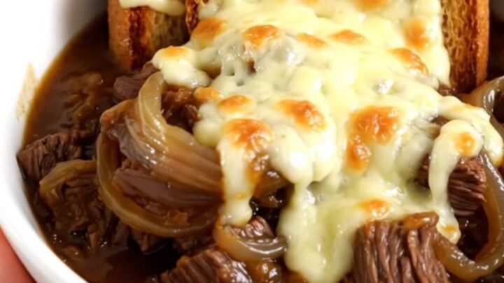A steaming bowl of French onion beef stew with tender beef, potatoes, and onions, topped with cheesy toast.