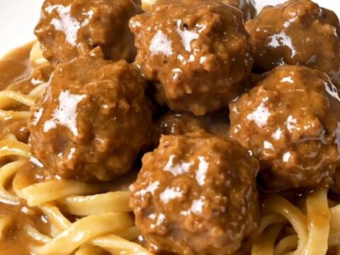 A top-down view of a black slow cooker filled with creamy Swedish turkey meatballs in a rich mushroom and brown gravy sauce.