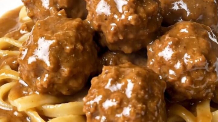 A top-down view of a black slow cooker filled with creamy Swedish turkey meatballs in a rich mushroom and brown gravy sauce.
