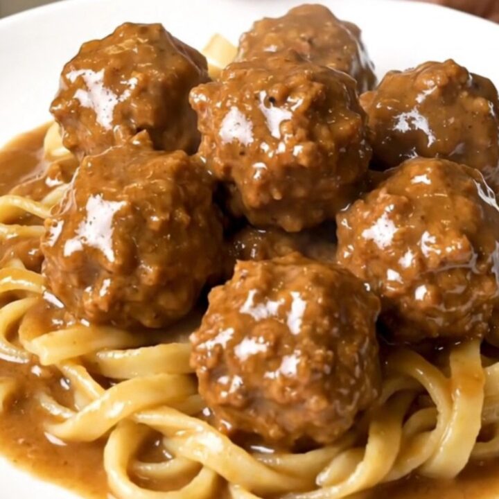 A top-down view of a black slow cooker filled with creamy Swedish turkey meatballs in a rich mushroom and brown gravy sauce.