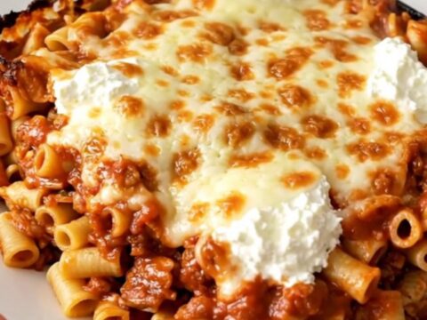 A slow cooker filled with cooked ziti, melted mozzarella, ricotta cheese, and fresh spinach.