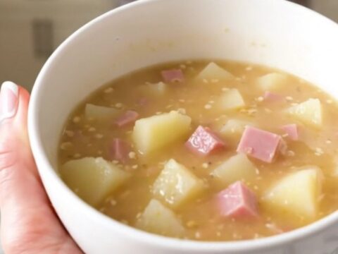 A steaming bowl of creamy Dijon ham and Swiss chowder topped with fresh herbs in a bright kitchen.