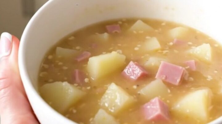 A steaming bowl of creamy Dijon ham and Swiss chowder topped with fresh herbs in a bright kitchen.
