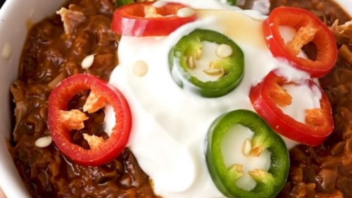 A white bowl filled with steaming turkey and black bean chili garnished with sour cream and fresh red chili slices.