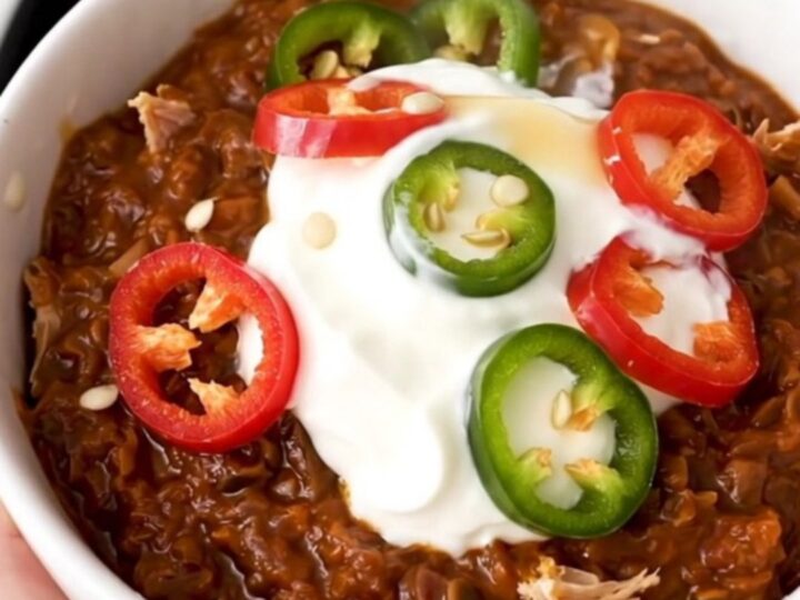 A white bowl filled with steaming turkey and black bean chili garnished with sour cream and fresh red chili slices.