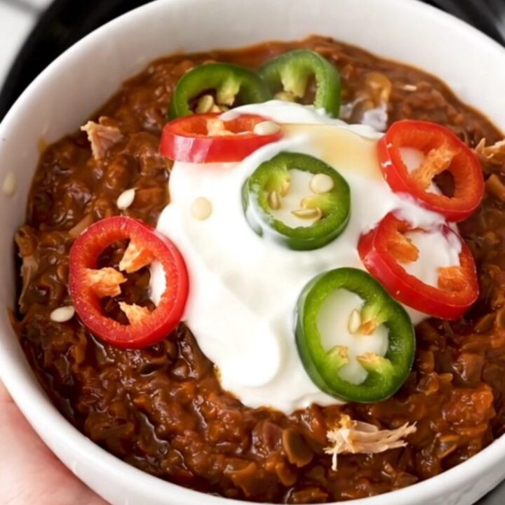 A white bowl filled with steaming turkey and black bean chili garnished with sour cream and fresh red chili slices.