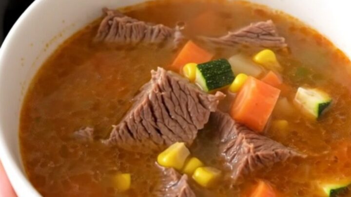A steaming bowl of Mexican Caldo de Res featuring tender beef chunks and colorful vegetables in a clear, rich broth.