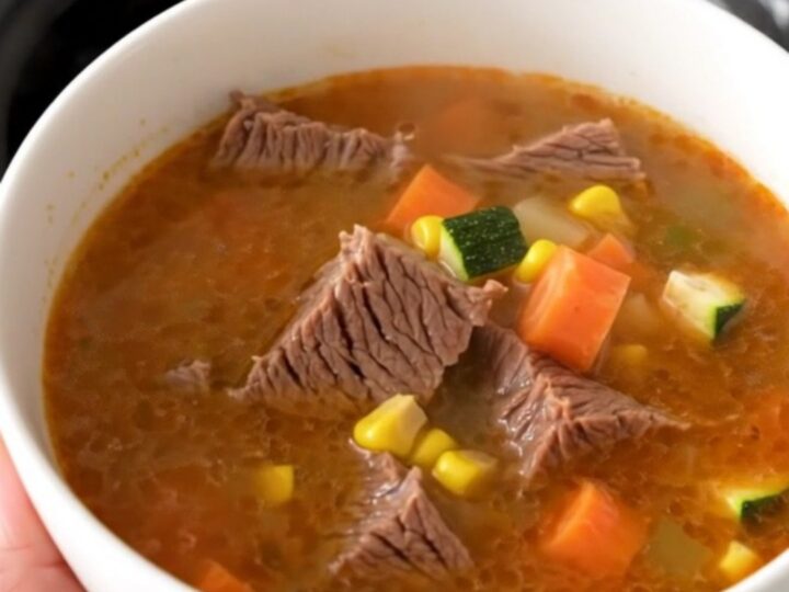 A steaming bowl of Mexican Caldo de Res featuring tender beef chunks and colorful vegetables in a clear, rich broth.