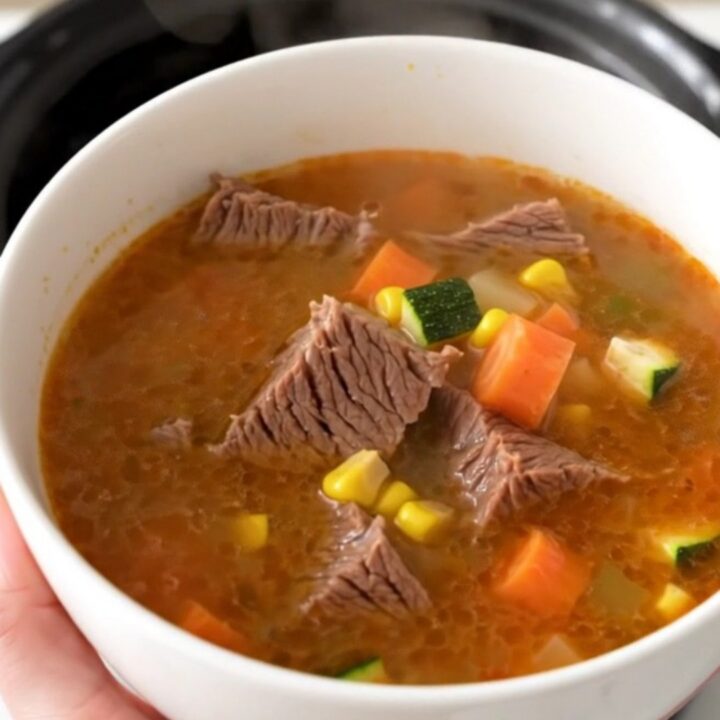 A steaming bowl of Mexican Caldo de Res featuring tender beef chunks and colorful vegetables in a clear, rich broth.