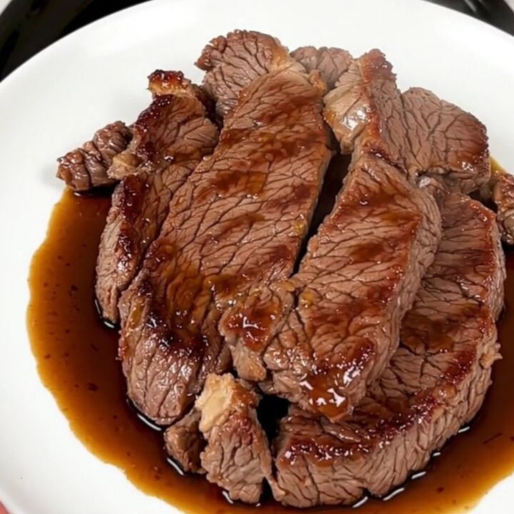 A glossy and tender ginger soy flank steak served on a white plate with a blurred kitchen background.