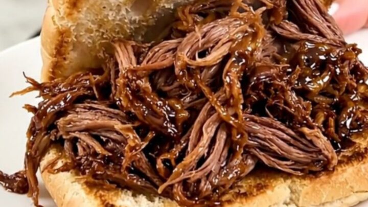 A slow cooker filled with tender, shredded honey balsamic beef on a kitchen counter.