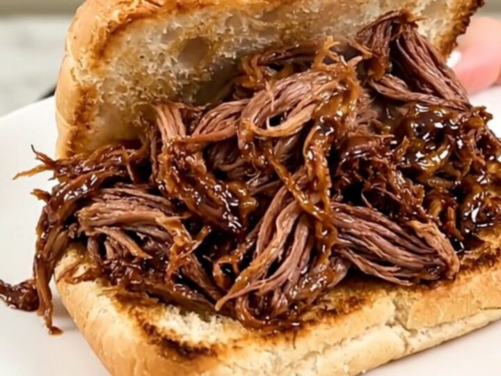 A slow cooker filled with tender, shredded honey balsamic beef on a kitchen counter.