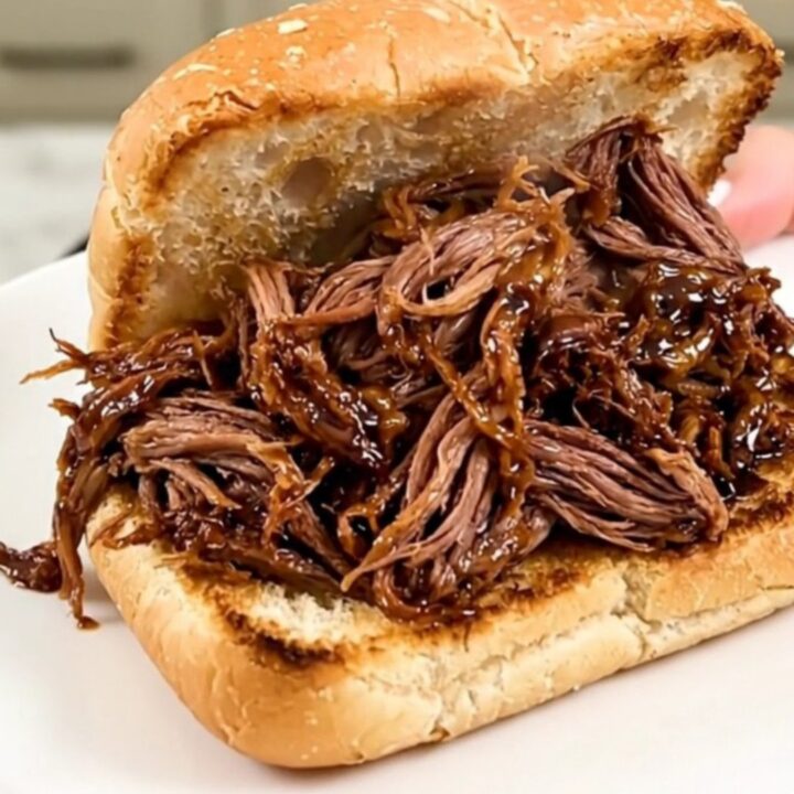 A slow cooker filled with tender, shredded honey balsamic beef on a kitchen counter.