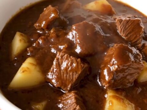 A white bowl filled with steaming, glossy beef stew featuring tender chunks of beef and potatoes in a rich barbecue glaze.