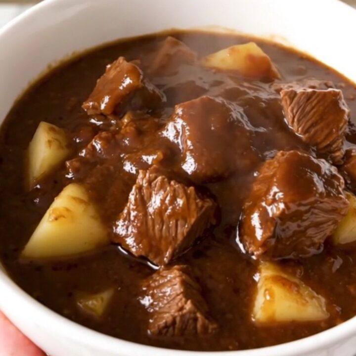 A white bowl filled with steaming, glossy beef stew featuring tender chunks of beef and potatoes in a rich barbecue glaze.