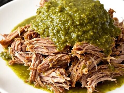 A close-up of tender, shredded salsa verde pulled pork on a white plate with a fork.