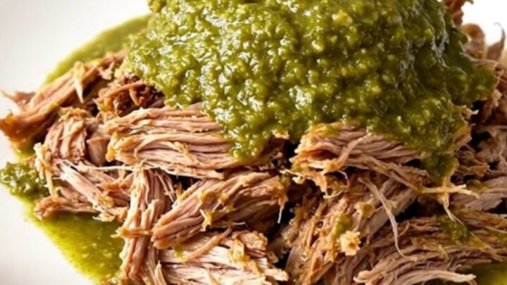 A close-up of tender, shredded salsa verde pulled pork on a white plate with a fork.