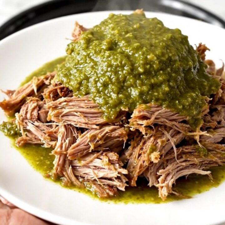 A close-up of tender, shredded salsa verde pulled pork on a white plate with a fork.