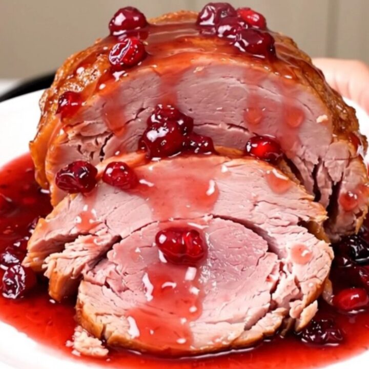 A close-up of a tender, glazed ham in a slow cooker with a ruby-red cranberry coating.