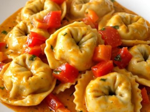 A top-down view of a slow cooker filled with creamy roasted red pepper tortellini before serving.