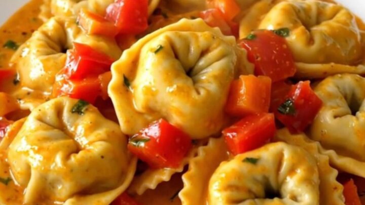 A top-down view of a slow cooker filled with creamy roasted red pepper tortellini before serving.