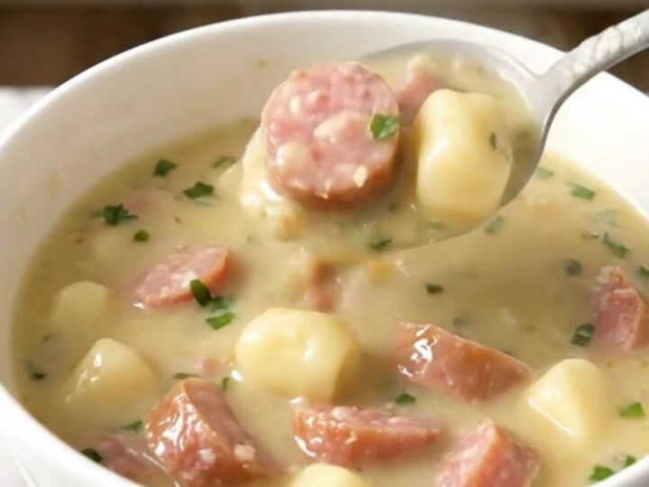 A steaming bowl of creamy garlic parmesan gnocchi soup with crumbled Italian sausage, photographed from a 45-degree angle.