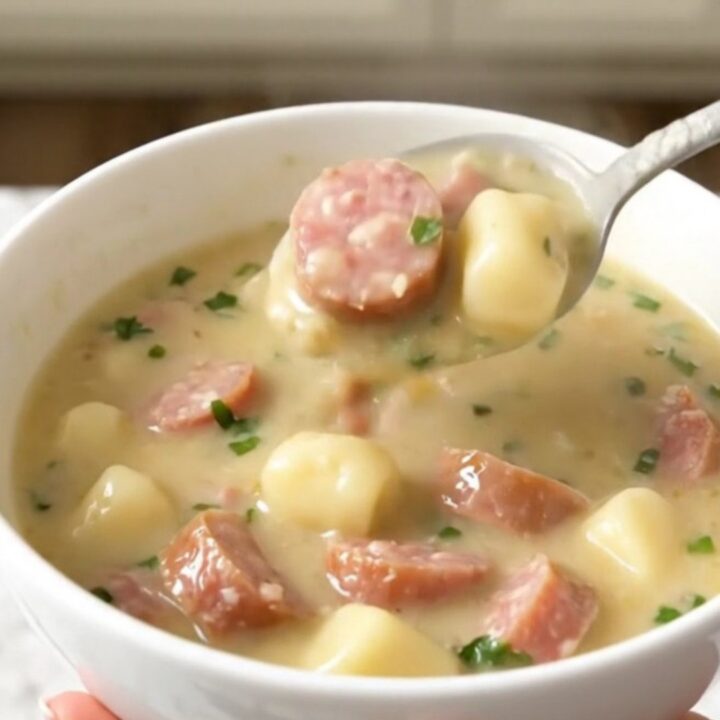 A steaming bowl of creamy garlic parmesan gnocchi soup with crumbled Italian sausage, photographed from a 45-degree angle.