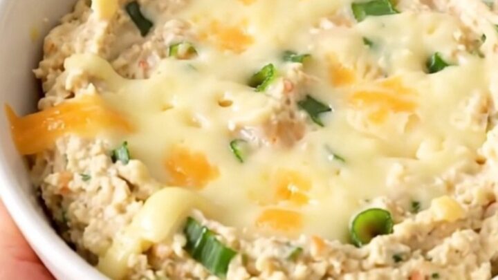 A warm, creamy roasted garlic and parmesan dip in a black slow cooker on a white countertop.