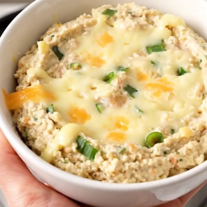 A warm, creamy roasted garlic and parmesan dip in a black slow cooker on a white countertop.
