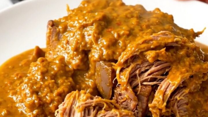 A close-up of a tender, shredded beef pot roast glazed in a rich, orange-tinted spiced pumpkin sauce on a white plate.