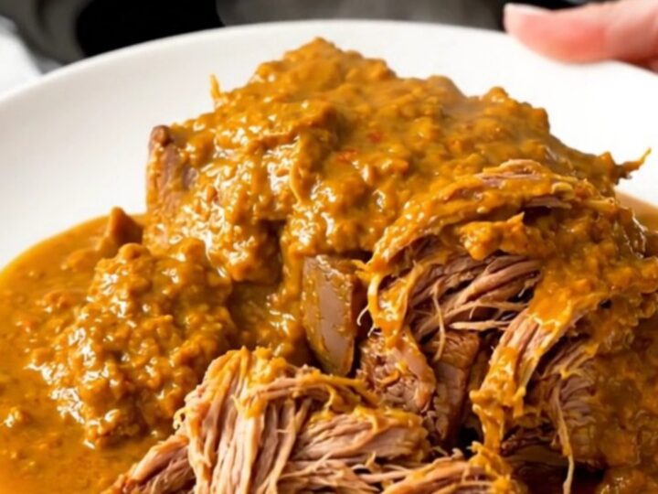 A close-up of a tender, shredded beef pot roast glazed in a rich, orange-tinted spiced pumpkin sauce on a white plate.