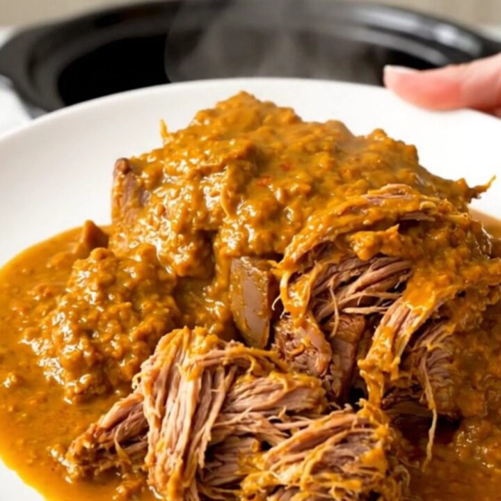 A close-up of a tender, shredded beef pot roast glazed in a rich, orange-tinted spiced pumpkin sauce on a white plate.