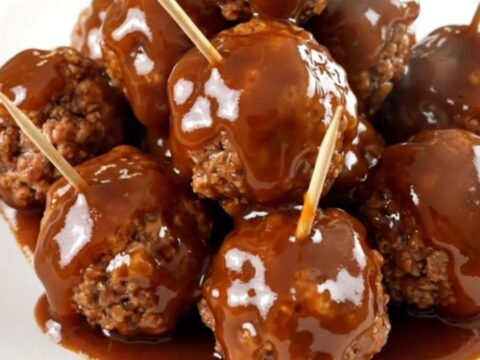 A close-up view of glazed beef meatballs in a slow cooker topped with a rich, glossy barbecue and apple butter sauce.