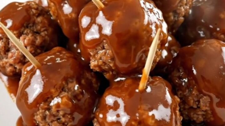A close-up view of glazed beef meatballs in a slow cooker topped with a rich, glossy barbecue and apple butter sauce.