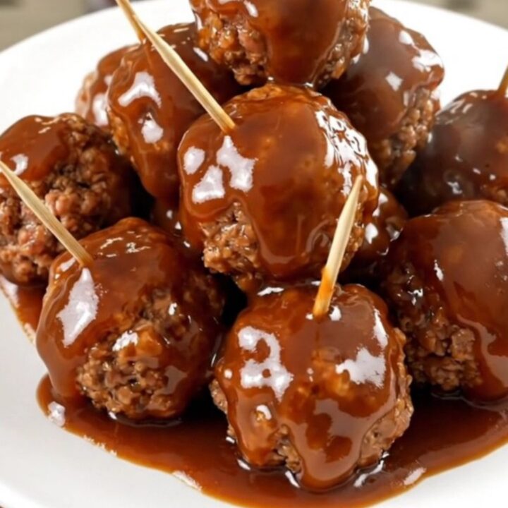 A close-up view of glazed beef meatballs in a slow cooker topped with a rich, glossy barbecue and apple butter sauce.