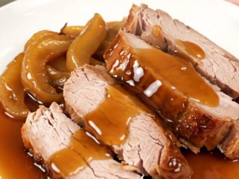 A slow cooker apple maple pork roast served on a white plate with glazed apple slices.