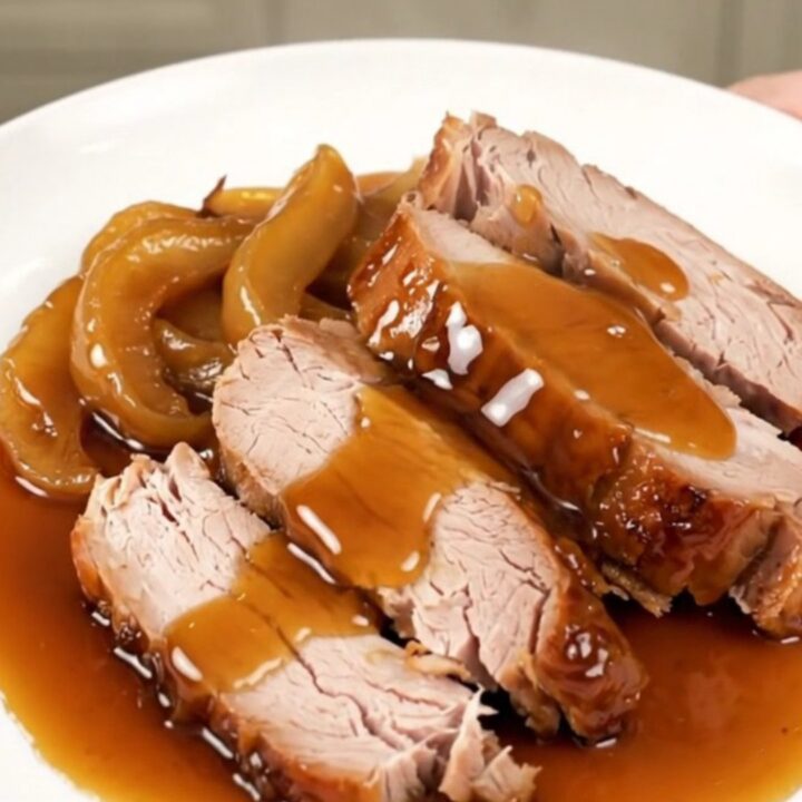 A slow cooker apple maple pork roast served on a white plate with glazed apple slices.