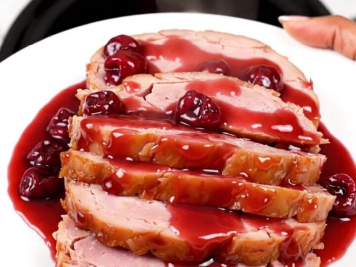 A close-up of a perfectly glazed spiral ham with a rich, glossy cherry sauce in a slow cooker.