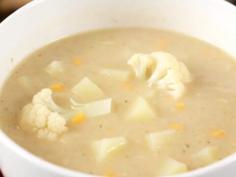 A steaming bowl of creamy white cauliflower soup served in a white bowl on a bright kitchen counter.