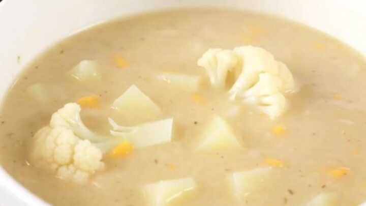 A steaming bowl of creamy white cauliflower soup served in a white bowl on a bright kitchen counter.