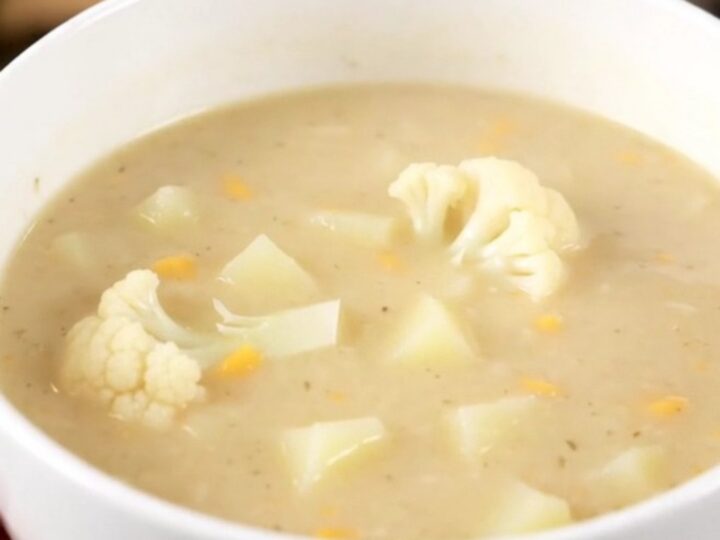 A steaming bowl of creamy white cauliflower soup served in a white bowl on a bright kitchen counter.