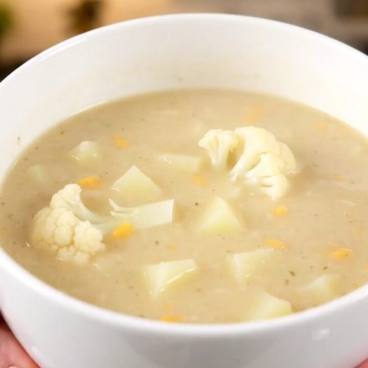 A steaming bowl of creamy white cauliflower soup served in a white bowl on a bright kitchen counter.