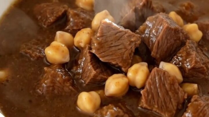 A white bowl filled with steaming beef and chickpea stew, showing tender meat and whole chickpeas in a rich brown sauce.