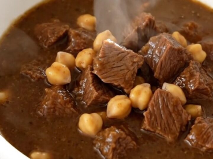 A white bowl filled with steaming beef and chickpea stew, showing tender meat and whole chickpeas in a rich brown sauce.
