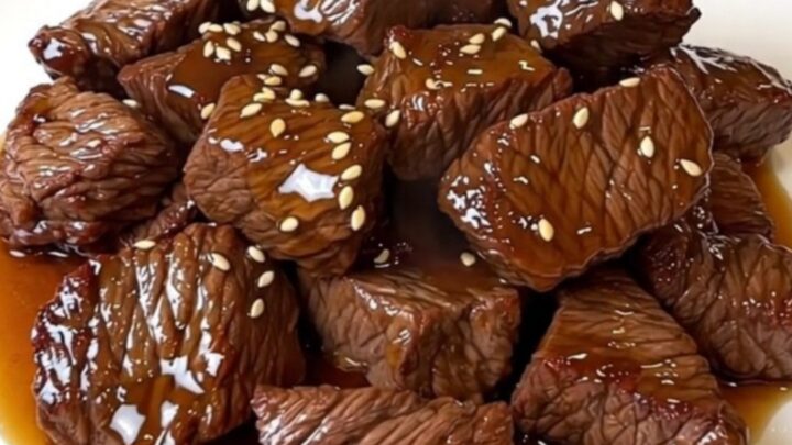A close-up view of glossy honey sesame beef served on a white plate.