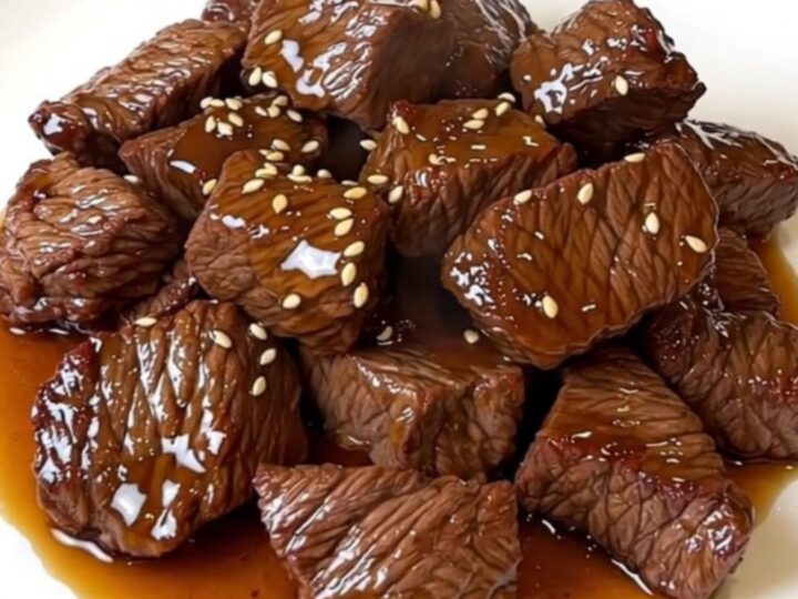 A close-up view of glossy honey sesame beef served on a white plate.