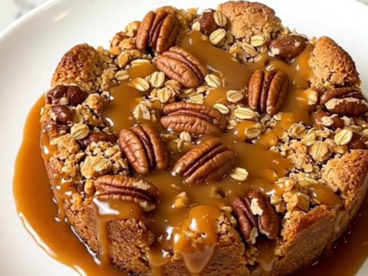 A close-up of a warm, golden caramel apple pecan crisp served on a white plate.
