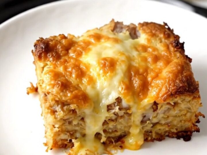 A warm, hearty breakfast casserole served on a white plate with visible hash browns, vegetables, and melted cheese.